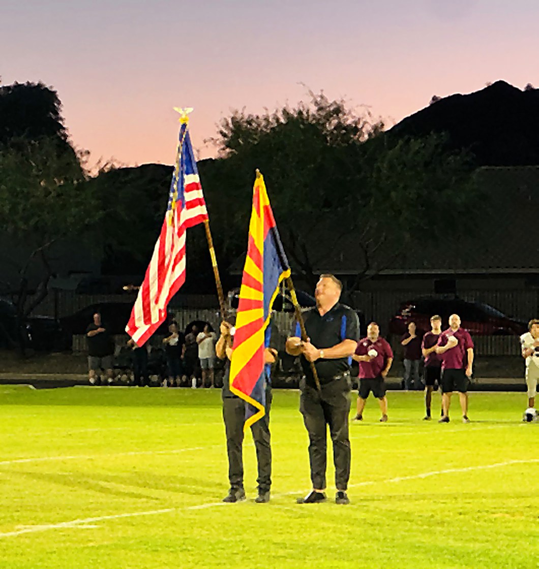 Two Elks carry the American and Arizona flags onto the field at the North Phoenix Prep homecoming game at dusk.