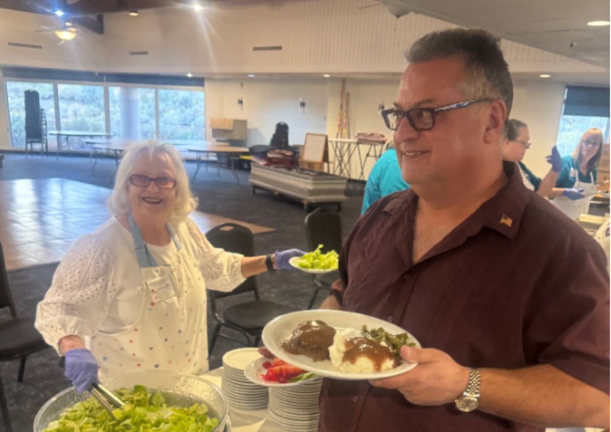 A volunteer serves dinner plates to a smiling member at Old Timers Night