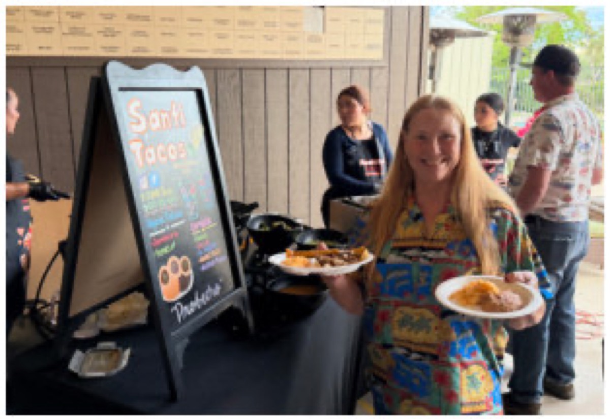A guest holding plates of food beside the Santi Tacos serving station